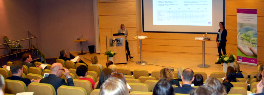 Bild från en föreläsningssal med två kvinnor på scenen och personer i publiken. 