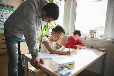 Male teacher teaches children at school desk
