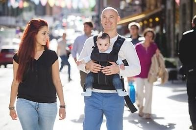 Two parents are out walking and the father is carrying the child in a carrier.