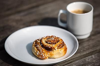 A cinnamon bun on a platter with a hot beverage next to it.