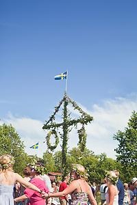 A group of people celebrate Midsummer by dancing around a Midsummer pole. 