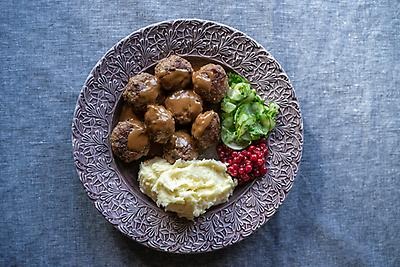 Plate with mashed potatoes, meatballs, lingonberries and pickled cucumber salad. 