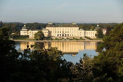 Drottningholms slott, kungafamiljens privata bostad. Bilden visar ett slott med skog omkring och en stor sjö framför. 