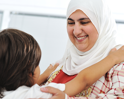 Smiling woman in a white hijab hugging a child.