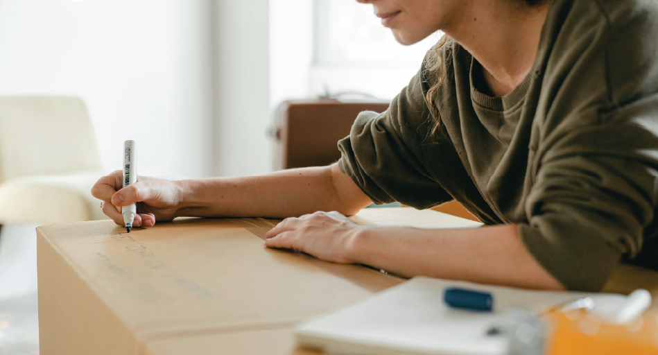 Kvinna som märker en flyttkartong genom att skriva på den, som förberedelse inför flytt.